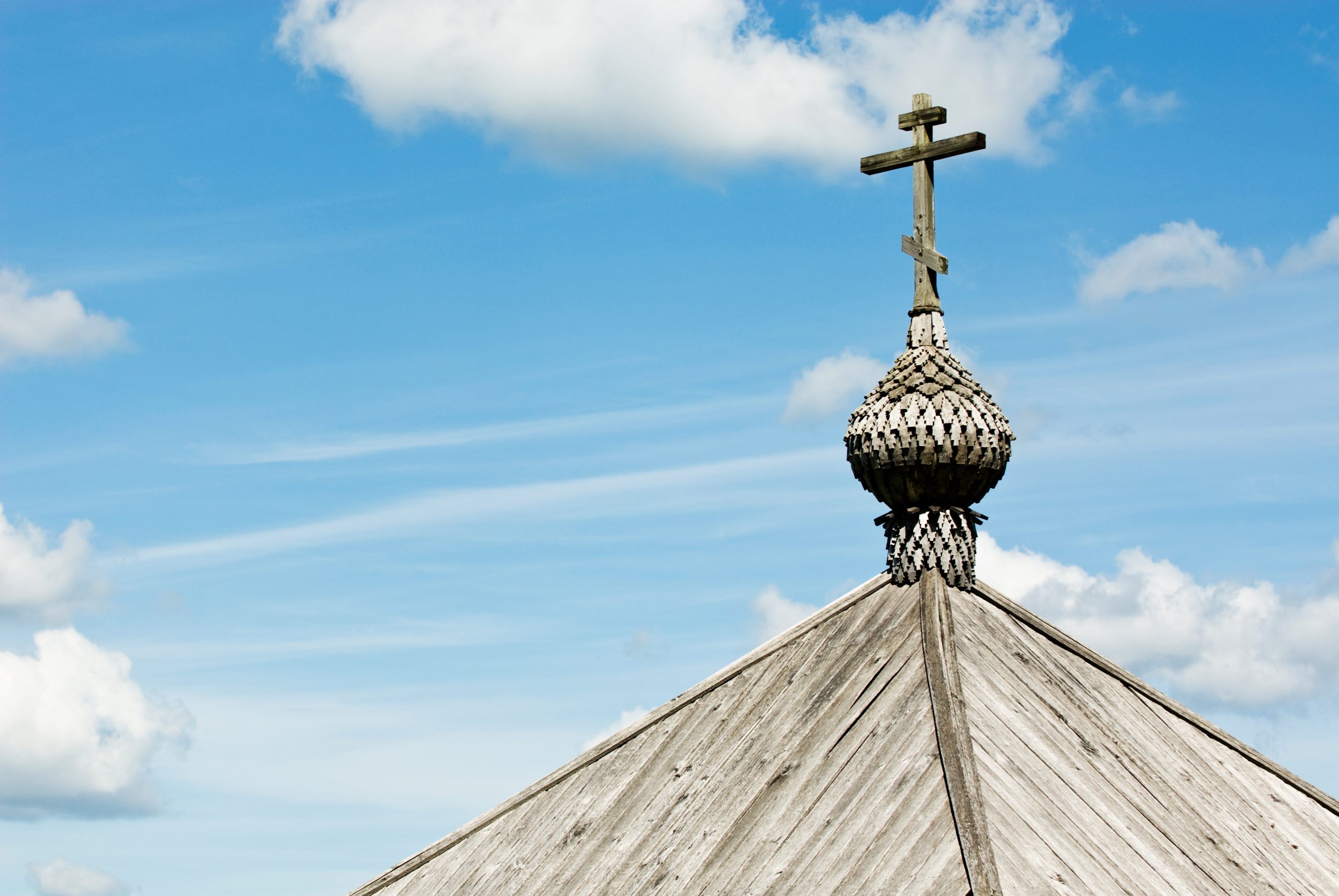 Roof of a wooden shrine with a cross over a blue sky