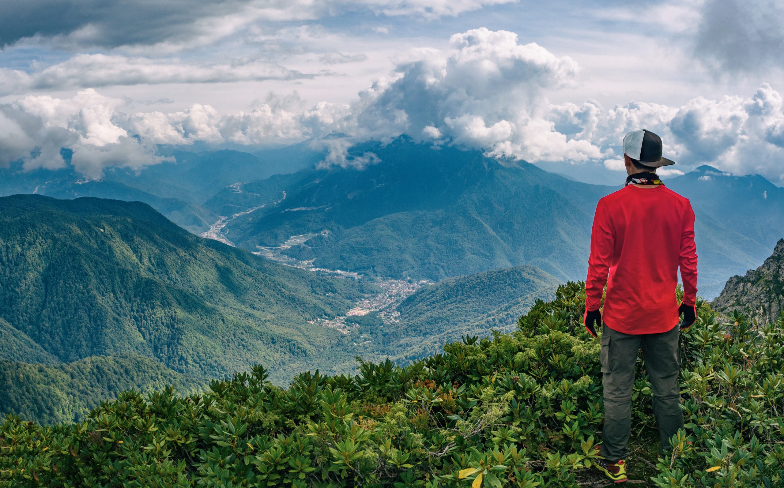 Young active man standing at panoramic background of mountains in Krasnaya polyana, Sochi (Russia)